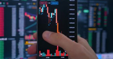 Akıllı telefonu elinde tutan tüccar yatırımcı finansal kripto hisse senedi fiyatlarını analiz ediyor. Kripto yatırımcısı, borsa finans ekranının önünde şifreli para almak için akıllı telefon uygulaması kullanıyor.. 