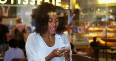Bir kahve dükkanının penceresinden, Afro-Amerikalı güzel bir kadın mutlu olurken akıllı telefonundan haber akışını kontrol ediyor. Elini yanağına koyuyor, neşe içinde..