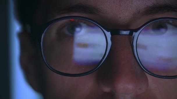自宅で夜にインターネット上のソーシャルネットワークを閲覧する眼鏡の男のクローズアップ コンピュータモニターは彼の眼鏡に反映されます メガネのインターネットユーザーを持つ男は夜にオンラインでコンピュータを使用します — ストック動画