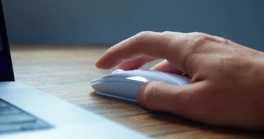 Close up of mans hand using white computer mouse to work at computer. Man businessman click computer mouse and scroll internet websites online on a work desk. Concept of working with laptop.