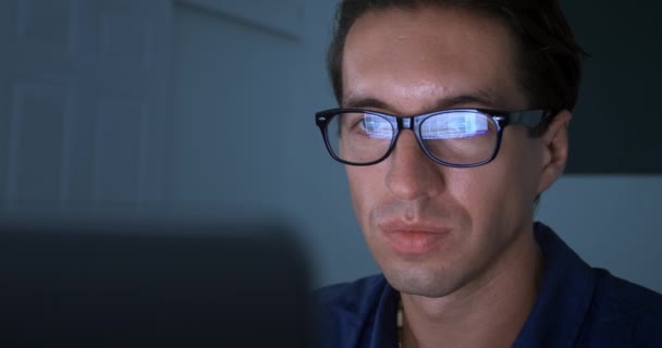 戴眼镜的男人的画像用笔记本电脑 在网上搜索信息 在网上滚动网站和社交网站 深夜在家里用男人的眼镜来反映笔记本电脑 — 图库视频影像