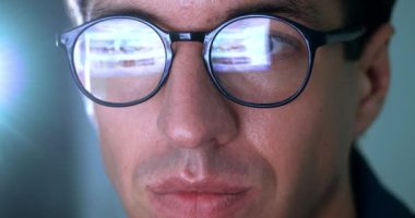 Close up portrait man in glasses using laptop, searching information on Internet pages, scrolling websites and social networks online, reflection of a laptop on glasses of a man, late at night at home