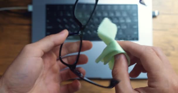男性の手のクローズアップは コンピュータで作業する前にメガネを拭く トップビュー 男性ビジネスマンはノートパソコンで仕事の準備をしています 彼のコンピュータのメガネを拭く オフィスで — ストック動画