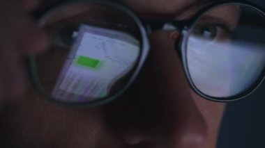 Business person working at laptop at late at night looking at monitor screen, reflections in eyeglasses. Person stock market trader using laptop computer at home office. Stock exchange trading concept