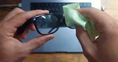 Close-up of male hands clean his glasses before working at the laptop, top view. Male student is preparing for work at a laptop, wipes his computer glasses, at home desk workplace.