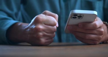 Close-up stressed man uses smartphone and loses his temper reading bad news on the internet, hits his fist on the table. Stressed male violently slams his fist on the table, showing anger