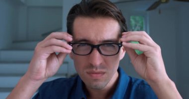 Student with bad eyesight puts on glasses to see better indoors. Close up male student looking and unable to read the text without the help of glasses on background of home office. Poor vision concept