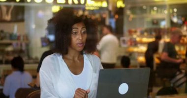 African American pretty woman, sitting at a table in a coffee shop, talking with her friends via video link.