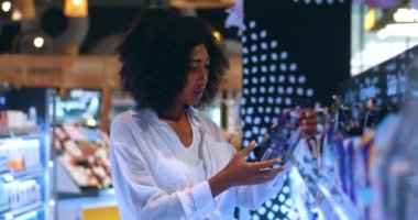 Young conscious woman carefully reads the contents of products on label, examine the merchandise presented on the shelf