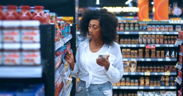 アフリカ系アメリカ人女性は彼女の現代のスマートフォンのリストをチェックし スーパーマーケットの食料品部門で健康食品を選択します — ストック動画