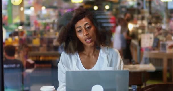 ラップトップでリモートで働く魅力的なアフリカ系アメリカ人の若いビジネス女性のコーヒーハウスの窓から眺め モダンなカフェでカップから熱い飲み物を飲みます リモートオンラインビジネス — ストック動画