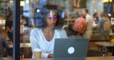 Pleasant charming and confident African American businesswoman in white shirt, typing text on the laptop keyboard, working remotely, communicating online with colleagues or business partners, in cafe.