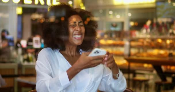 幸せなアフリカ系アメリカ人女性は カフェに座っている間 携帯電話を使用して成功した勝者 素晴らしいニュースを読み 拳をきれいにし 興奮とモバイル宝くじの喜びを感じます — ストック動画
