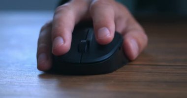 Close-up of a mans hand using a black computer mouse at a wooden table. Closeup male hand scrolling wheel and clicking buttons with computer mouse. The concept of working on laptop computer.