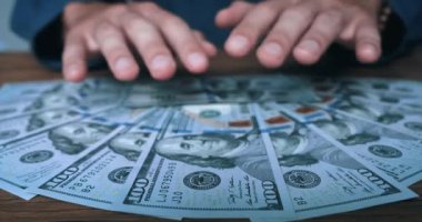 Close-up of greedy mans hands grabbing a bunch of dollars lying on the table. The man takes his money, American dollars from the table. Concept of making money and easy profit. Male win money cash.