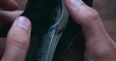 Close-up of a man opening a wallet filled with US 100 dollar bills and counting the money. Male hands count money cash in the wallet, extreme close up. Concept of money and wealth.