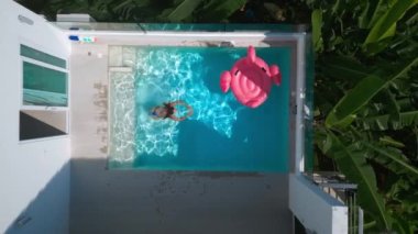 Aerial view female tourist enjoying swimming at vacations at small swimming pool. Female tourist chilling on summer vacations at resort with swimming pool at hot sunny day, top view. Drone shot