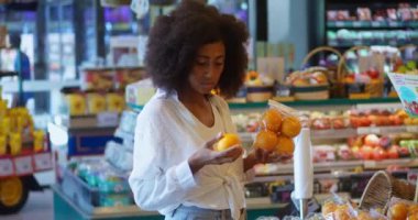 African American woman, vegetarian shopper consumer chooses healthy tasty organic fruits, holding juicy and ripe oranges