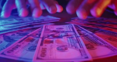 Close up lucky male winner hands grabbing bunch of dollars lying on casino table in neon light. Happy winner received winnings money at casino. Man win cash money in gambling or lottery. Easy money.