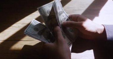 Close-up of American US dollars in hands, counting money. Business person sitting at the table, counts earned money, fixing profits. Business man calculates 100 usd banknotes in hands.