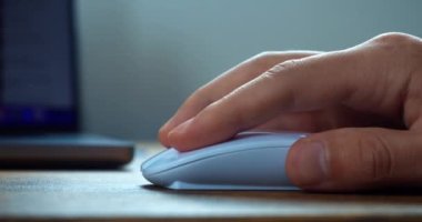 Clicking white computer mouse on a work desk. Human hand holding using mice for working online. Working with laptop computer using wireless handheld pointing device.