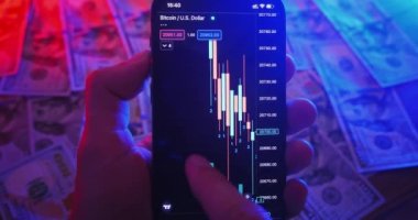 Cryptocurrency earning concept. Mobile trading cryptocurrency market analysis. Close-up person pro trader using mobile phone app analyzes crypto market, investing in crypto, money on table background.
