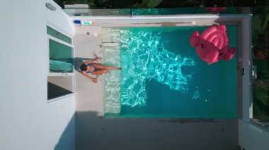 Aerial drone view female tourist chilling near swimming pool at hotel resort on holidays. Top view young female sunbathing, chill and relax at holidays near small private pool