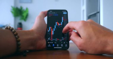 Close up crypto trader investor broker using smartphone app analyzing financial stock market price on smartphone, checking online trading platform application, buying cryptocurrency at home kitchen.