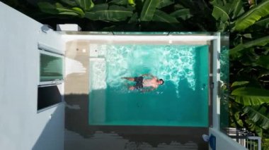 Top view of young male enjoying resting in small private swimming pool enjoying sunbathing and vacations in tropical destination, aerial view. Male traveling in holidays vacations on tropical resort.