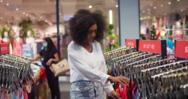 African American millennial female in casual shirt and denim jeans, shopping for new suitable stylish clothes in fashion store. Young female shopping fashion style in clothing store.