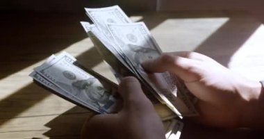 Counting hundred dollar banknotes on wooden table in ray of light. Male hands counting money cash paper money. Close up male hands counting 100 USD dollar bills. Business, finance, economy concept