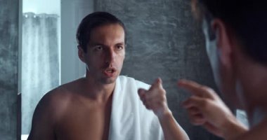 Serious man motivate himself to pull himself together before difficult day, standing in bath in morning and looking in mirror. Man in bath talking to himself motivating himself for new working day