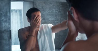 Headshot of depressed young man looking in the bathroom mirror. Depressed man cries and covers his face with his hand alone in the bathroom in the morning. Concept of male grief, broken man.