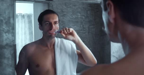 Young Man Brushing Teeth Bathroom Man Towel Shoulder Looks Mirror — Αρχείο Βίντεο