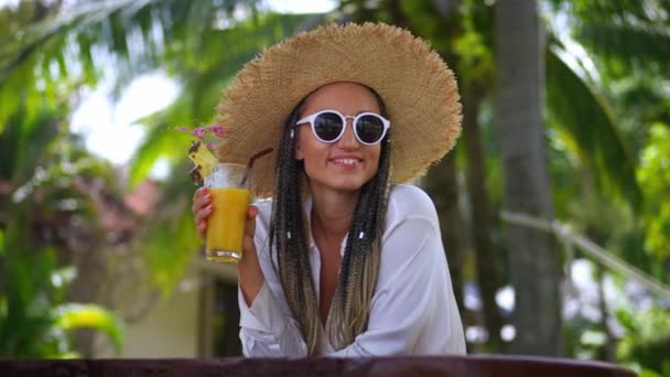 特写年轻 面带微笑的女游客 35岁 戴着太阳镜 头戴一顶帽子 喝橙汁 暑假享受奢华假期 冷却和休息的概念 — 图库视频影像