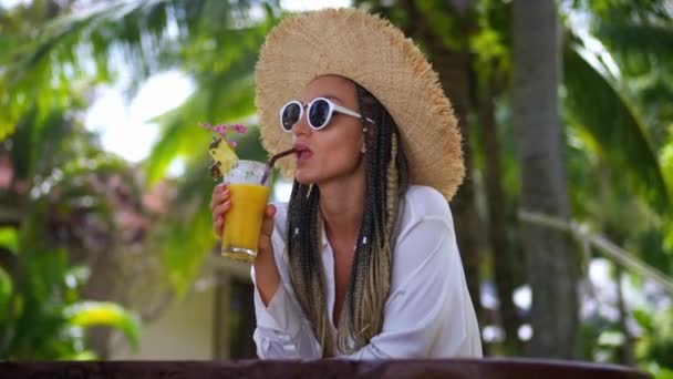 近照年轻快乐的女游客戴着太阳镜 头戴一顶帽子 喝着橙汁 令人毛骨悚然地享受着夏天的奢华假期 野外地方咖啡馆的女游客冷 — 图库视频影像