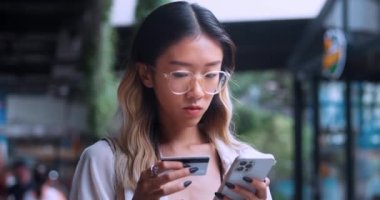 Şehirdeki alışveriş merkezinin yakınında elinde kredi kartı ve akıllı telefon tutan Asyalı güzel bir bayan. İnternetten akıllı telefon alan Asyalı bayan alışverişçi. E-bankacılık uygulaması.