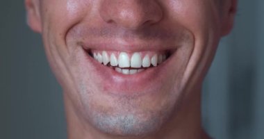 Extreme close up of young mans mouth smiling with teeth. Happy positive man is smiling indoors, macro shot. Detail of a smile man