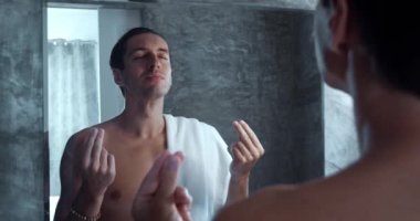 Man meditates while standing in front of mirror in bath. Young millennial male getting ready for new day, looking at himself in mirror, meditating and motivating himself in the morning in the bath.