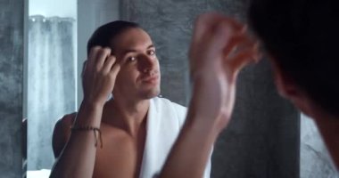 Happy caucasian man looking in the mirror in the bathroom, combing his hair with his fingers, starting for new day, enjoying male beauty morning routine in the bathroom. Man in bath with towel.