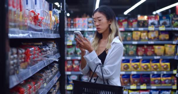 Nakupování Supermarketu Asijská Žena Nakupující Dívá Smartphonu Kontroluje Ceny Produktů — Stock video
