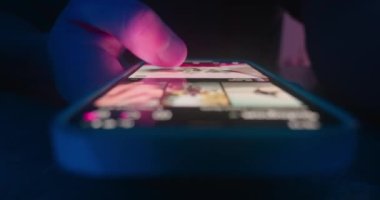 Close up of mans hand holding smartphone, flipping through social network, likes, at night. Close-up male scrolling internet social media feed using smartphone. Concept of virtual life in smartphone.