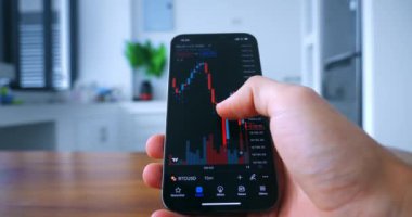 Male hand holds smartphone, analyzes the crypto stock market, for the purchase of cryptocurrency on stock exchange, at home in the kitchen. Trading using smartphone for analyzing stock market.