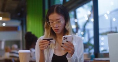 Asian lady credit card holder use mobile phone pay online buy consumer goods order services on ecommerce websites from cafe. Female make safe transaction with credit card and mobile phone at ebank app