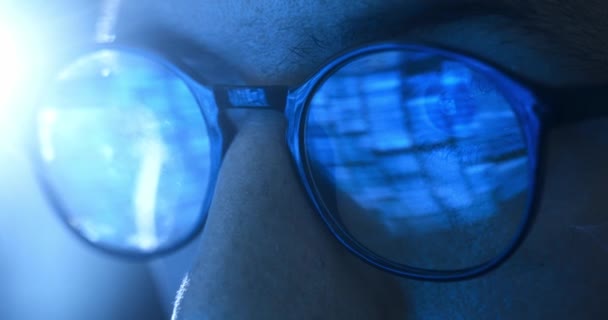 夜にコンピュータで働いている男プログラマーの眼鏡のクローズアップ目は バイナリコードのモニターが彼の眼鏡に反映されます メガネのコンサートプログラマーは 夜にコンピュータで動作します — ストック動画
