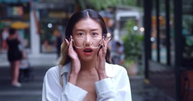 Şaşırmış Asyalı kadın şok oldu. Kameraya bak, gözlükleri çıkarıyor. Asyalı bir kadının gözlüklü portresi. Gördüklerine hayran kalmış ve diş telleriyle gülümsüyor. Alışveriş merkezinde duruyor..