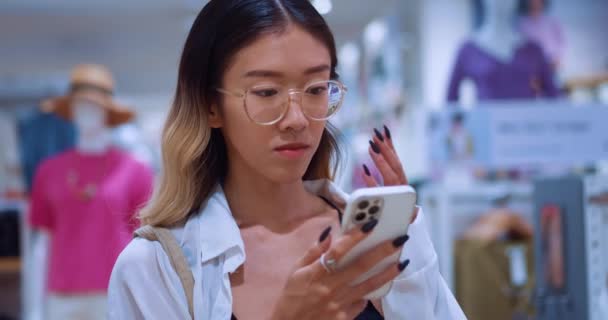 Азійська Жінка Стоїть Магазині Одягу Дивиться Мобільний Телефон Читає Відгуки — стокове відео