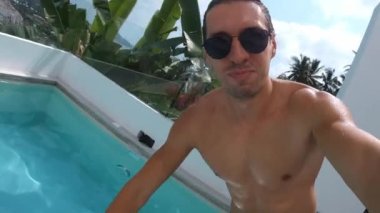 Komik adam, yaz tatilinin tadını çıkarırken kendini kameraya çekerek tropikal bir ülkede tatilin tadını çıkarıyor. Tatillerde bilardoda zıplayan gözlüklü bir erkek. Selfie POV çekimi.