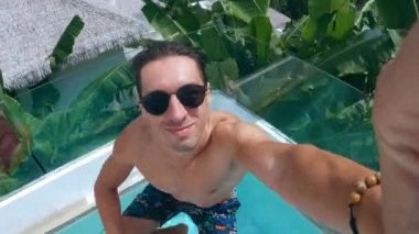 Genç adam gözlüğü, tropik bir ülkede yaz tatilinde havuza atlıyor. Milenyum erkeği yaz tatillerinde otel havuzunda aktif bir yaz tatili geçirir..