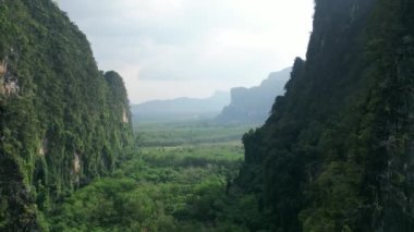 Hava aracı dağların arasından uçarak el değmemiş yeşil ormanın üzerinden geçiyor. Sinema videosu. Dünya 'nın doğal güzelliği. Tayland 'ın başkenti Krabi' de yeşil otantik orman üzerinde dağlık alanda sinematik video drone uçuşu.